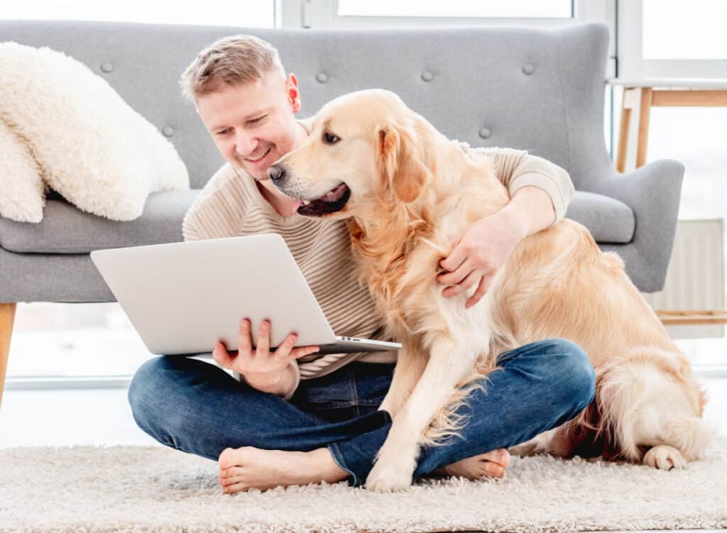 man sitting on the floor hugging dog both looking at a laptop